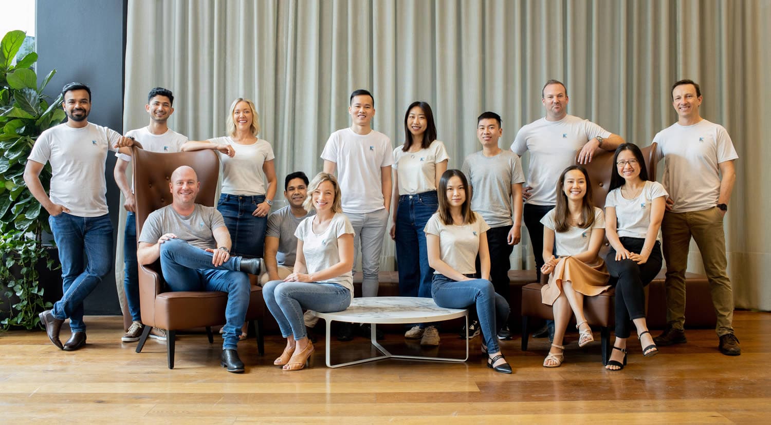 Team group photo featuring a diverse group of professionals in branded casual white t-shirts and jeans, posed in a modern indoor space with natural light, greenery, and elegant furniture. Captured by Hero Shot Photography, showcasing teamwork, diversity, and a friendly corporate culture.