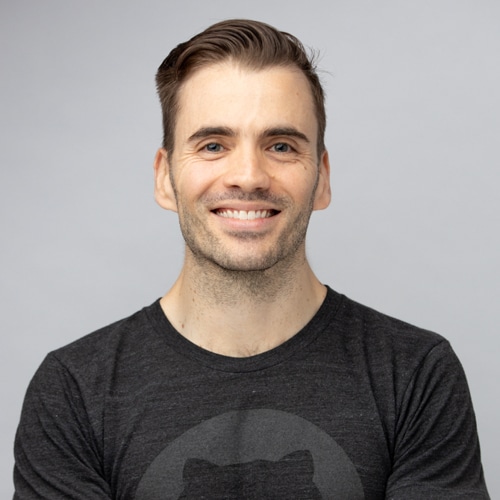 Professional portrait of a smiling man wearing a casual charcoal gray t-shirt, captured against a soft gray background by Hero Shot Photography. Reflects approachability, confidence, and modern branding ideal for personal profiles, creative industries, or casual corporate settings.